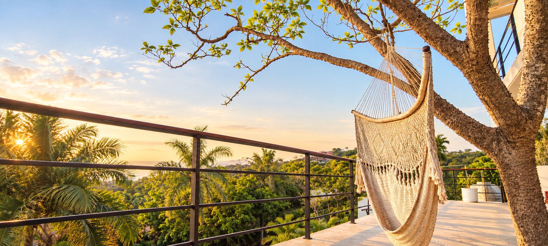 Eine Hängematte, die an einem Baum auf einem Balkon befestigt ist, mit Blick auf üppiges Grün und einen klaren Himmel.