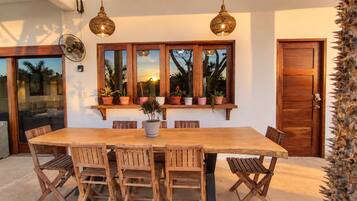 A dining area with a wooden table and chairs, a window with plants, and a door.