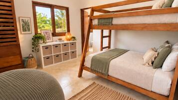 A bunk bed with a wooden frame, a bedside table with a lamp, and a view of greenery outside.