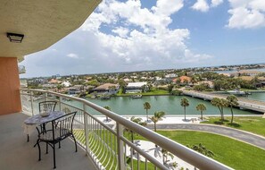 Ein Balkon mit Tisch und Stühlen, der auf einen Yachthafen mit Booten, eine Brücke und einen Wohnbereich mit Häusern und Grünflächen blickt.
