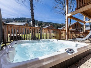 A hot tub in a wooden deck area with a view of cabins in the background. - One-bedroom Cabin (Sankt Georgen am Kreischberg)