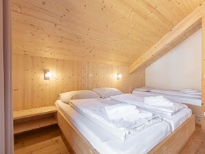 A wooden cabin room with two beds, each with white linens and towels, and two wall-mounted light fixtures. - One-bedroom Cabin (Sankt Georgen am Kreischberg)