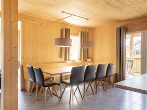 A wooden interior with a dining table and chairs, a hanging light fixture, and a view to the outside. - One-bedroom Cabin (Sankt Georgen am Kreischberg)
