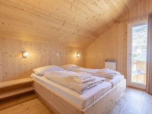 A wooden cabin bedroom with a bed, two bedside tables, and a window with a view of a snowy landscape. - One-bedroom Cabin (Sankt Georgen am Kreischberg)