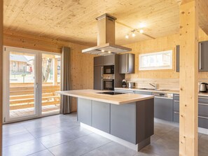 A modern kitchen with a central island, built-in appliances, and a view through a glass door. - One-bedroom Cabin (Sankt Georgen am Kreischberg)