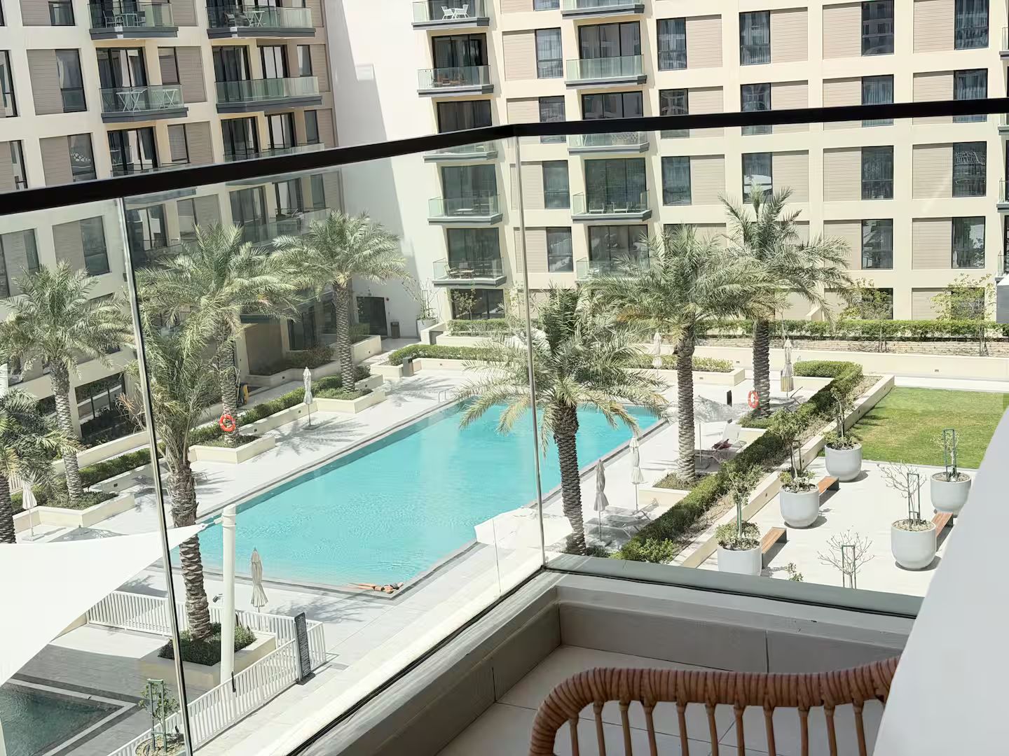 A residential building with a swimming pool, palm trees, and a balcony with a wicker chair.