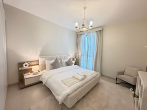 Un dormitorio moderno con una cama grande, mesitas de noche, una silla y una araña.