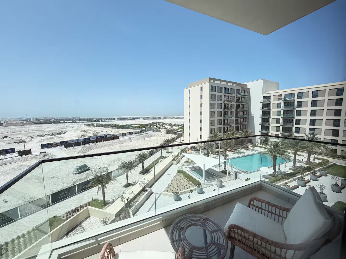 A balcony with a view of a swimming pool, palm trees, and a desert landscape.
