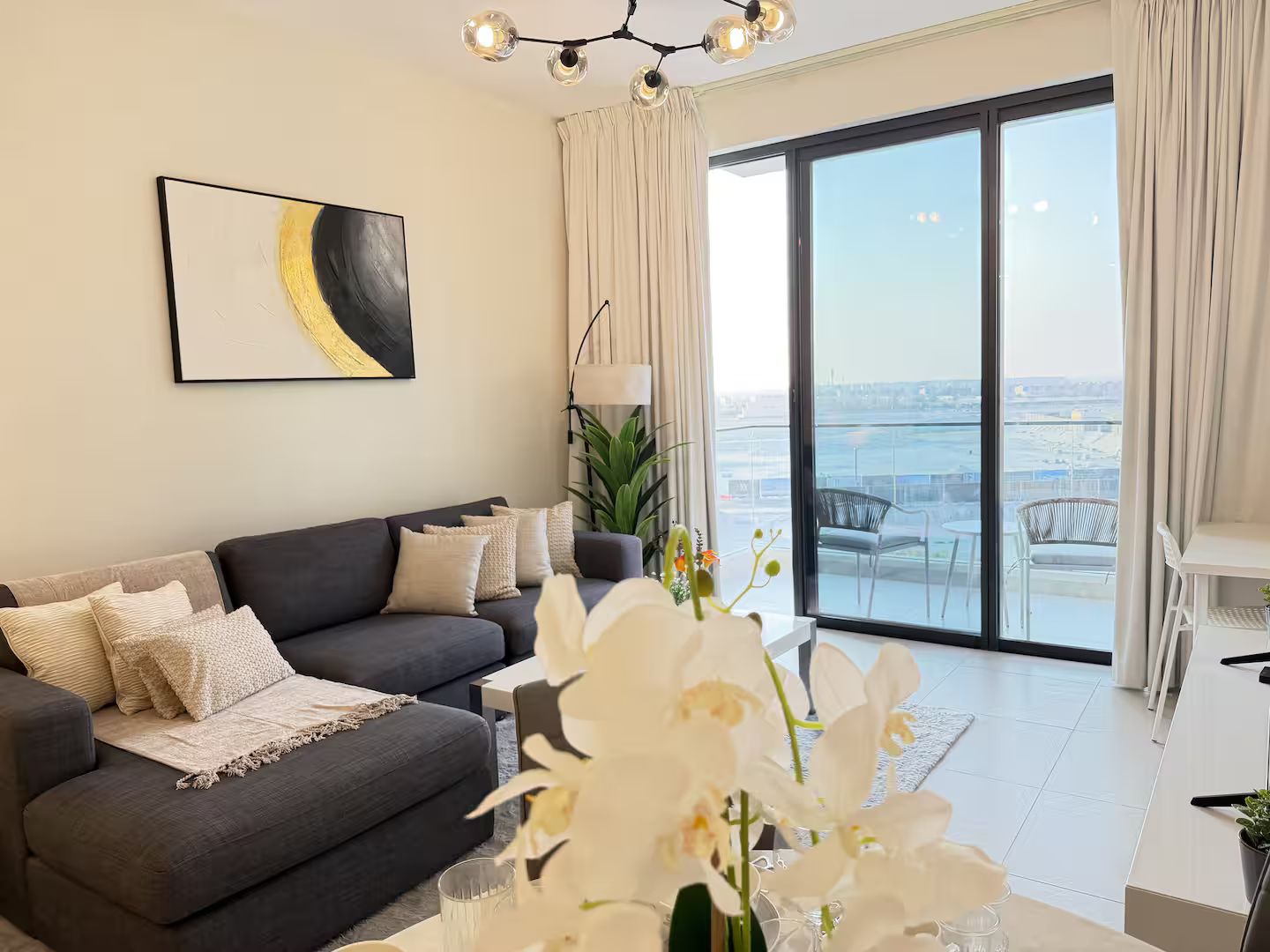 Ein modernes Wohnzimmer mit grauem Sofa, einem großen Fenster und Blick auf die Stadt sowie einem Kronleuchter.