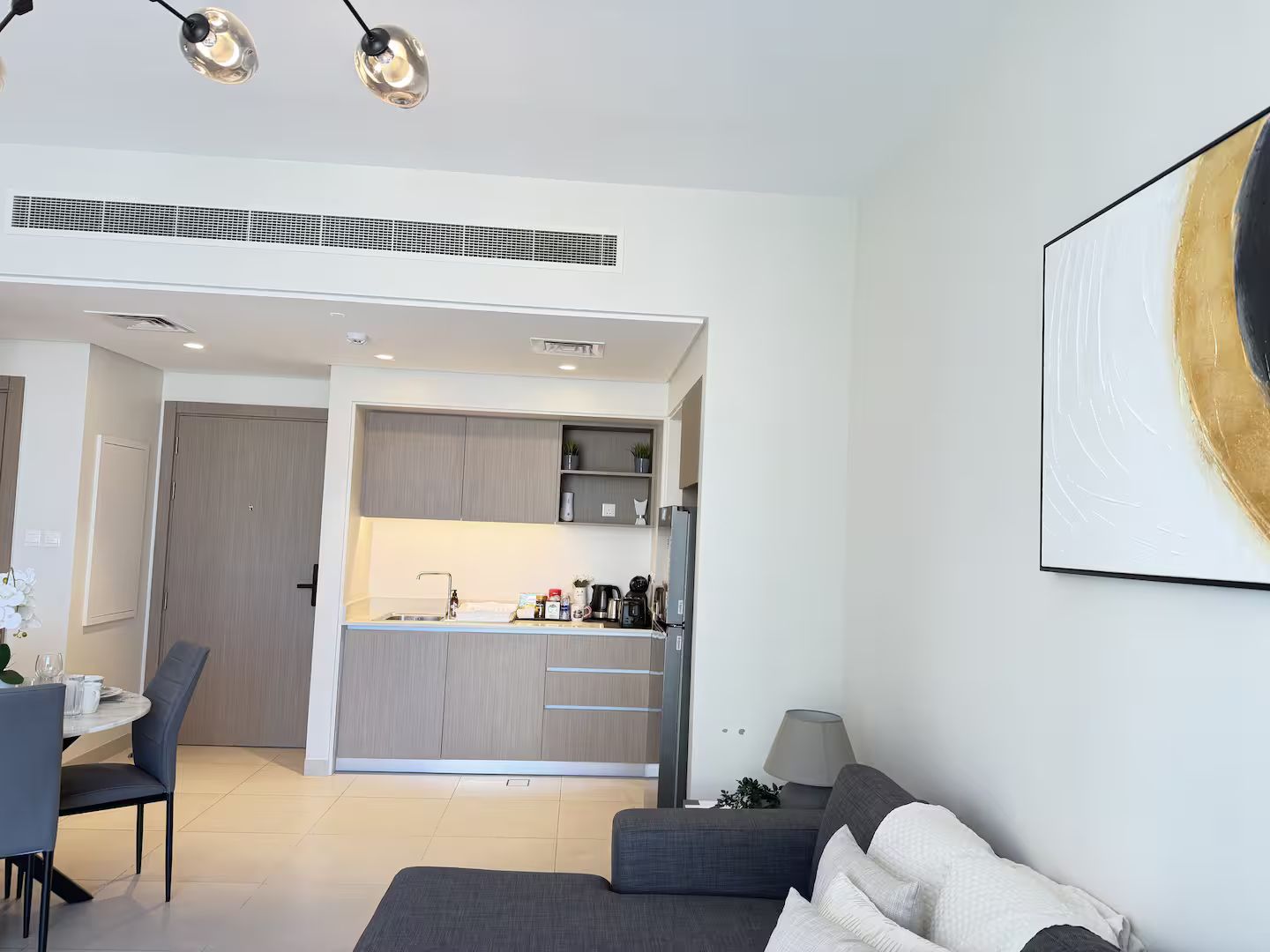 Una sala de estar moderna con un sofá gris, un comedor con una mesa y sillas, y una cocina con una isla integrada y electrodomésticos.