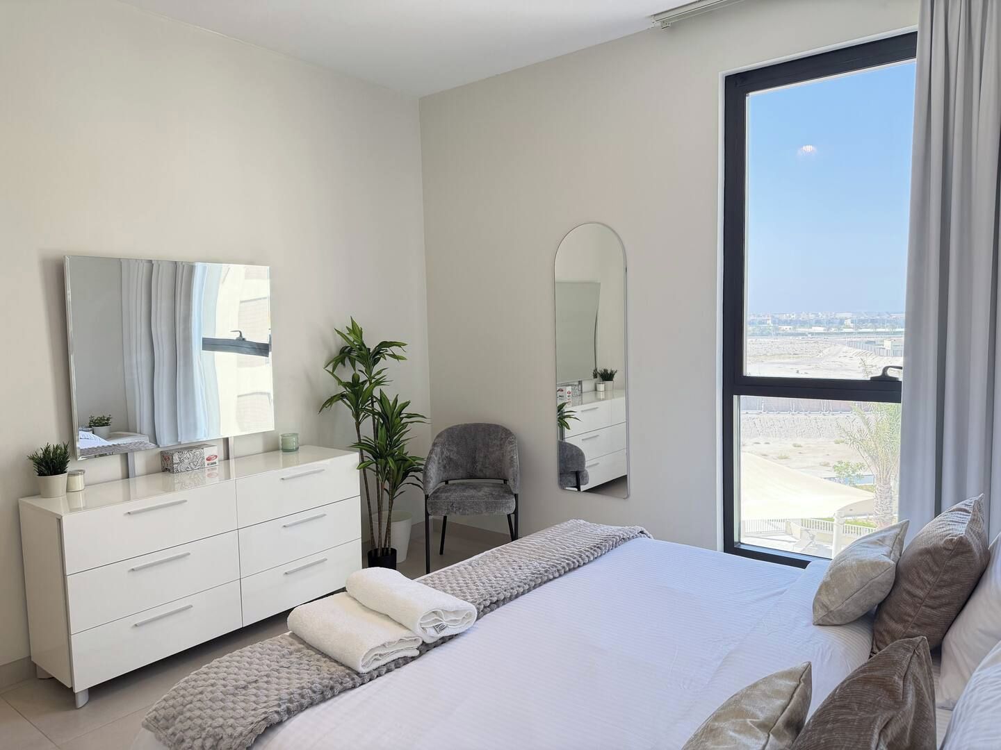 Une chambre moderne avec un grand lit, une commode, une chaise et une grande fenêtre donnant sur la ville.