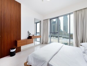 A modern bedroom with a large bed, a wooden console table, a mirror, and a view of a cityscape through large windows. - Bright Modern Retreat Along the Dubai Canal (Dubai)