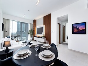 A modern living room with a dining area, large windows, a flat-screen TV, and a city view. - Bright Modern Retreat Along the Dubai Canal (Dubai)