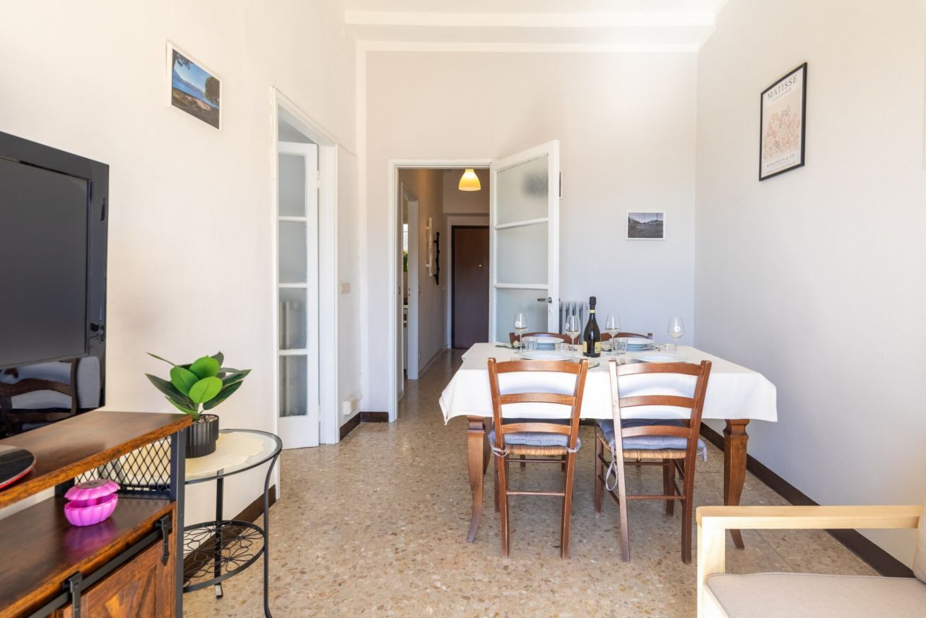 A dining area with a table set for four, chairs, a plant, and a TV on a stand.