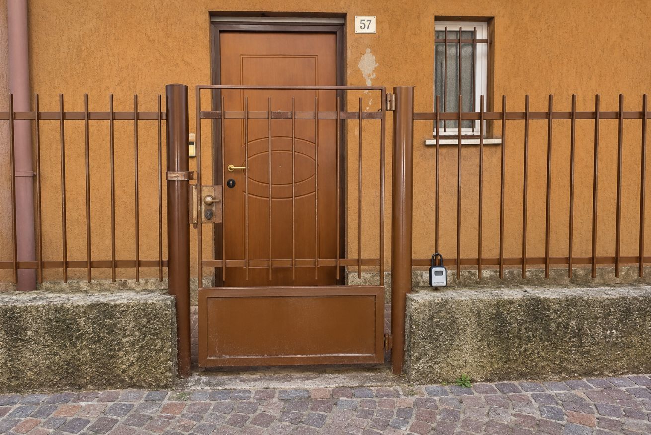 Ein verschlossener Eingangsbereich mit einer braunen Tür, einem Metallgitter und einem kleinen, vergitterten Fenster.