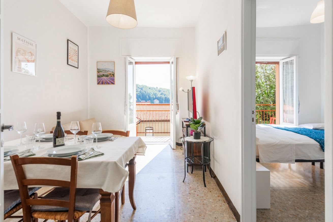 A dining area with a table set for two, a chair, a bottle of wine, and a painting on the wall.