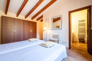 A bedroom with a large bed, a wardrobe, a chair, a mirror, and a bathroom visible through an open door. - Rapalin, Villa 5StarsHome Mallorca (Arta)
