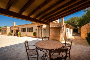 A covered patio with a round table and chairs, a stone floor, and buildings with traditional architecture. - Rapalin, Villa 5StarsHome Mallorca (Arta)