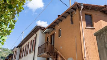 Ein Gebäude mit einer Treppe, die zu einem Balkon führt, einem Fenster mit Rollläden und einem sichtbaren Stromkabel.
