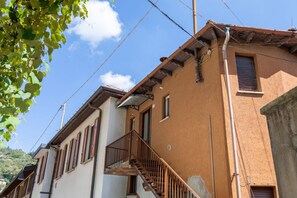 Ein Gebäude mit einer Treppe, die zu einem Balkon führt, einem Fenster mit Rollläden und einem sichtbaren Stromkabel.