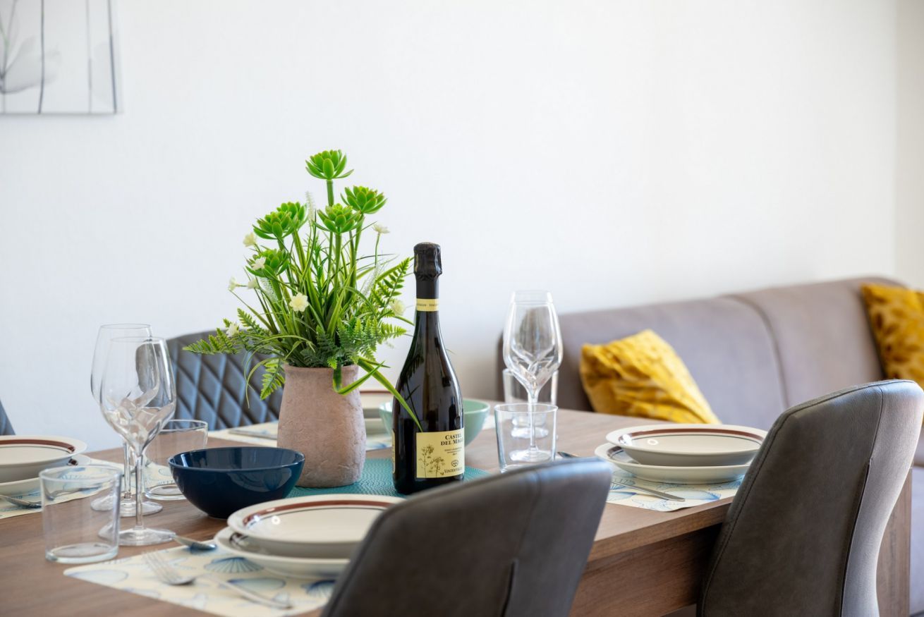 Une table à manger dressée avec des assiettes, des verres, une bouteille de vin et une plante en pot.