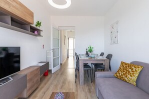 Ein modernes Wohnzimmer mit Flachbildfernseher, einer Couch, einem Esstisch mit Stühlen und einer Küchenzeile mit Kühlschrank.