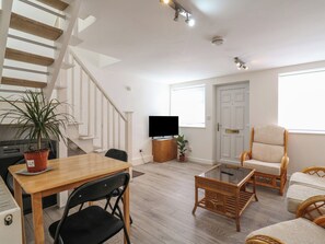 Ein Wohnzimmer mit einem Holzessttisch, schwarzen Stühlen, einem Glastisch, Korbmöbeln, einem Fernseher und einer Treppe.