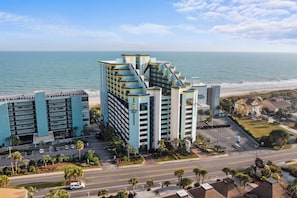 A multi-story hotel with a modern design, located near a beach with a view of the ocean.