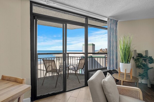 A balcony with a view of the sea, a dining table, and a seating area with chairs.