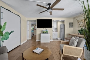 A living room with a flat-screen TV, a ceiling fan, a dining area with a table and chairs, and a kitchen with a refrigerator. - The Sea Suite  10th-Floor Corner Unit with Panoramic Ocean Views & Rooftop Pool (Myrtle Beach)