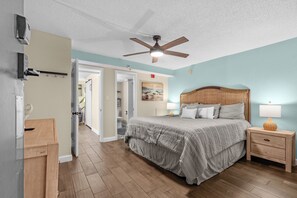 A bedroom with a bed, bedside table, lamp, ceiling fan, and a view of a bathroom. - The Sea Suite  10th-Floor Corner Unit with Panoramic Ocean Views & Rooftop Pool (Myrtle Beach)