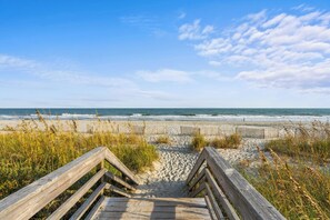 A wooden boardwalk leading to a beach with sand and grassy dunes.