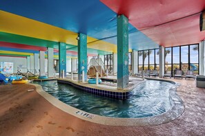 An indoor swimming pool with multiple lanes, a changing room, and a seating area with a view of palm trees.
