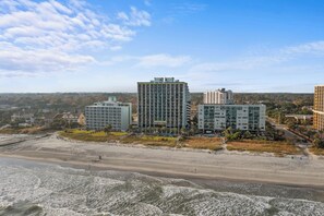A beachfront hotel with multiple high-rise buildings, a sandy beach, and a clear sky.
