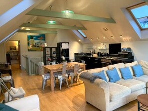 Geräumiges Loft mit Essbereich, Küche und Wohnzimmer, gekennzeichnet durch hohe Decken und Dachfenster.