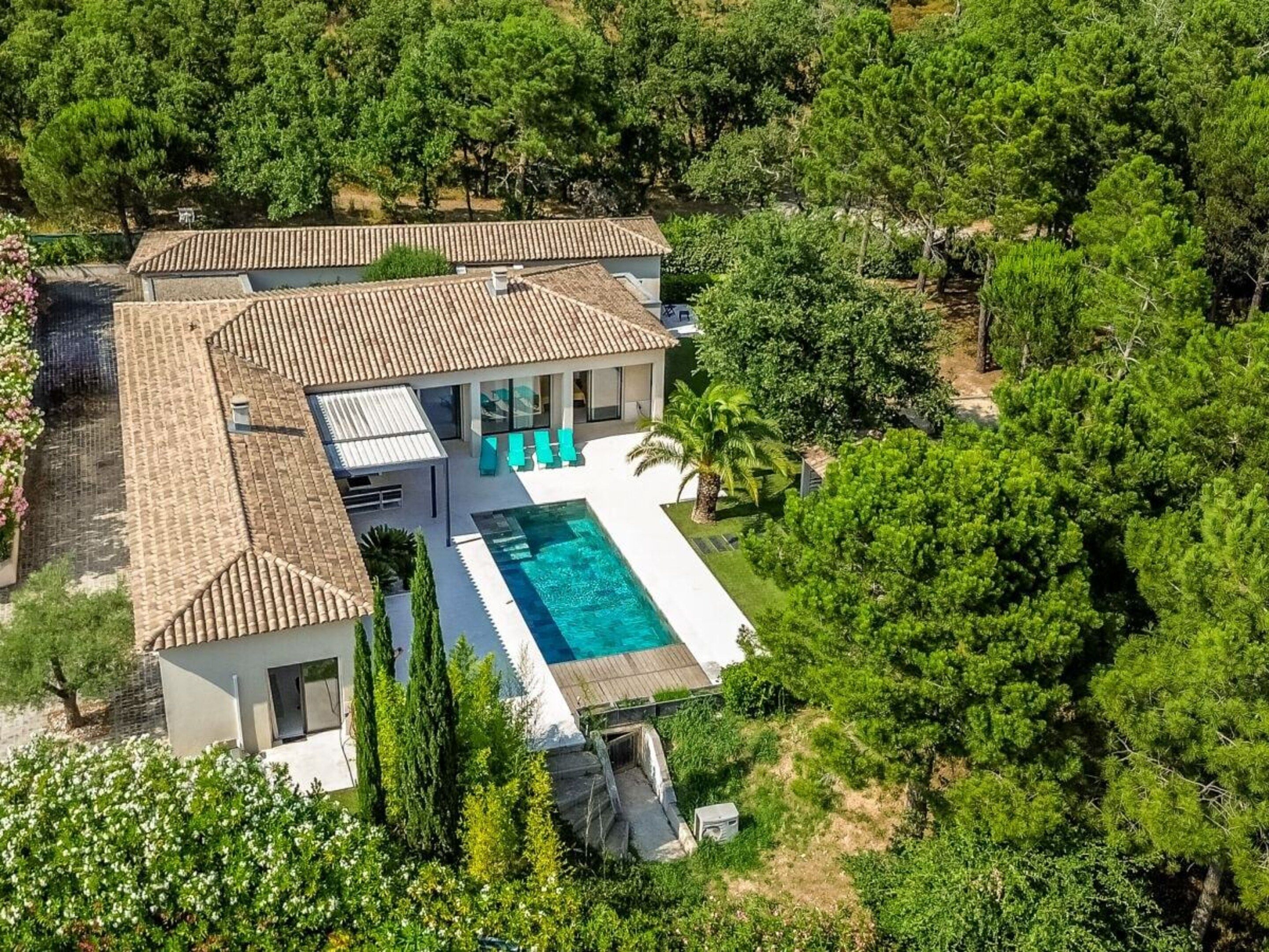 Eine moderne Villa mit Schwimmbad, umgeben von üppiger Vegetation und Bäumen.
