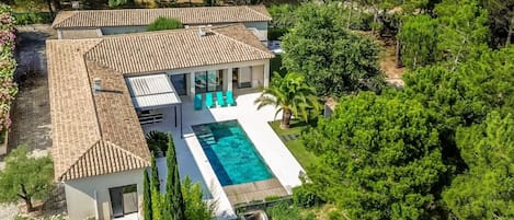 A modern villa with a swimming pool, surrounded by lush greenery and trees.