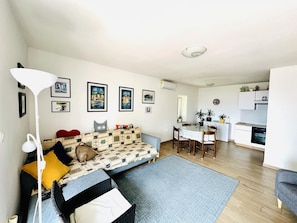 A living room with a sofa, a dining table with chairs, a kitchen area, and a ceiling light fixture. - Luxury 100 m2, 2-bedroom apartment with balcony & garden (Rijeka)