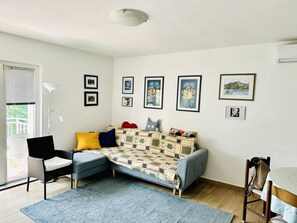 A living room with a sofa, a chair, a table, and a floor lamp. There are pictures on the wall and a window with blinds. - Luxury 100 m2, 2-bedroom apartment with balcony & garden (Rijeka)
