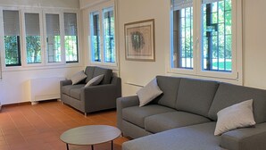A spacious living room with a grey sectional sofa, a round coffee table, and large windows with blinds. - Villanova 4 rooms (Villanova)