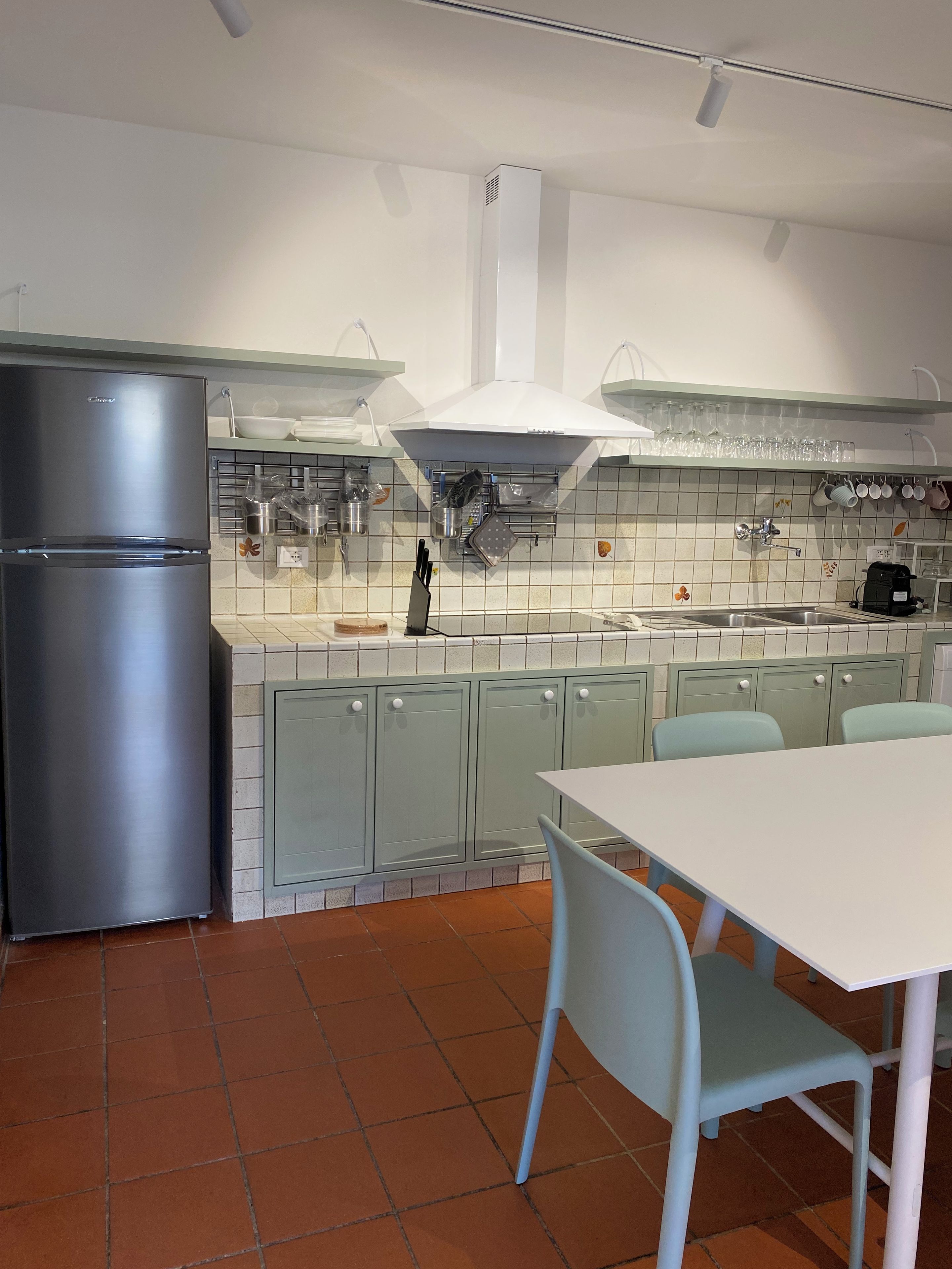 A modern kitchen with a stainless steel refrigerator, a white dining table with chairs, and a tiled backsplash.