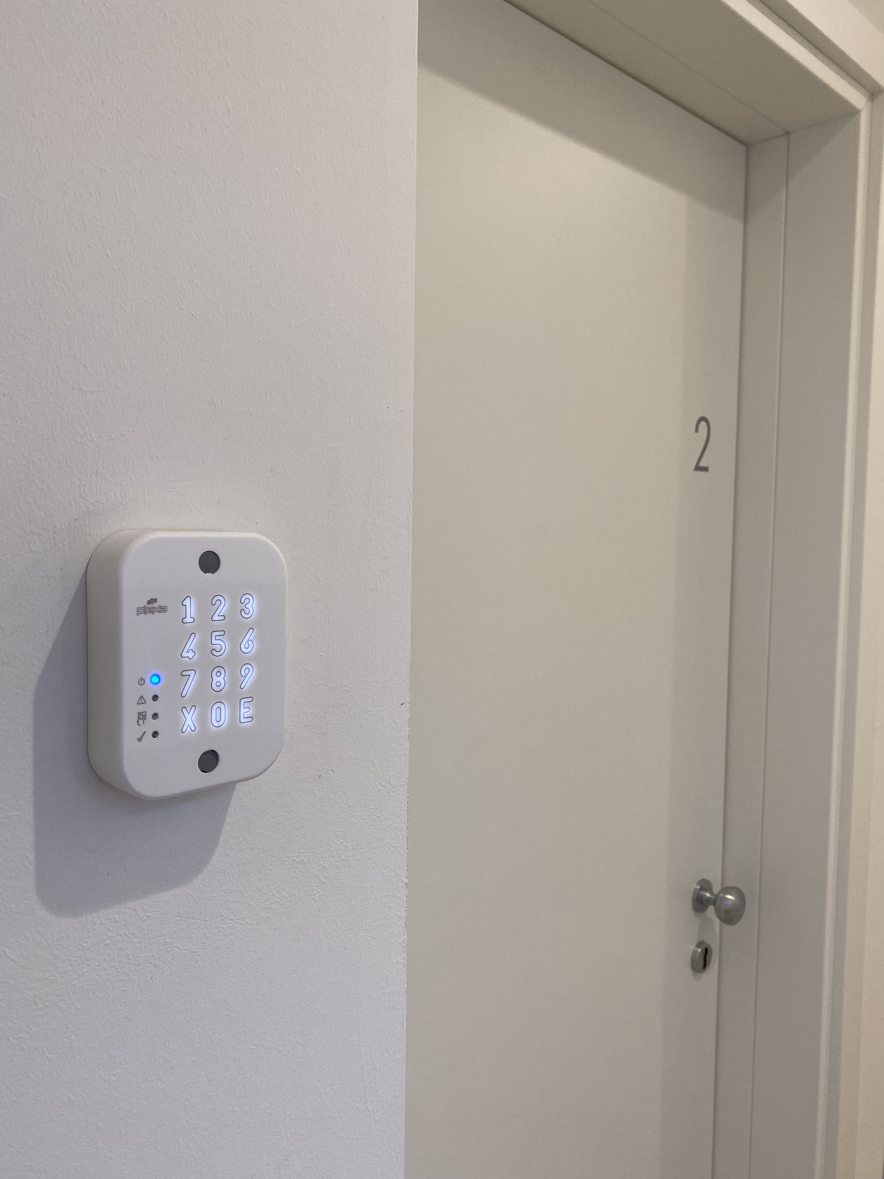 A wall-mounted electronic keypad lock on a white door with the number '2' above it.