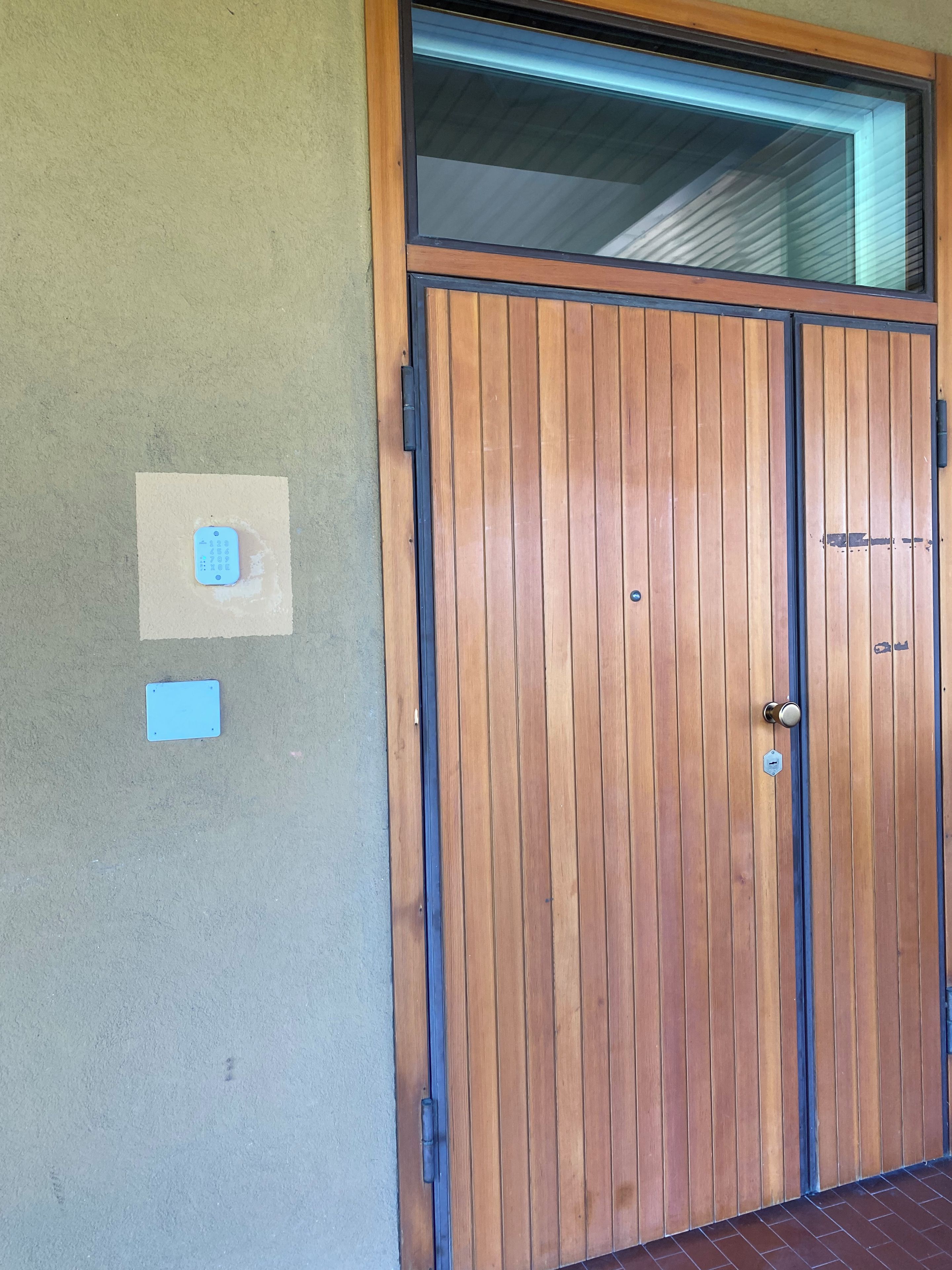 Une porte à deux battants en bois, dotée d’un trou de serrure et d’une poignée, une petite plaque bleue fixée au mur et une fenêtre au-dessus de la porte.