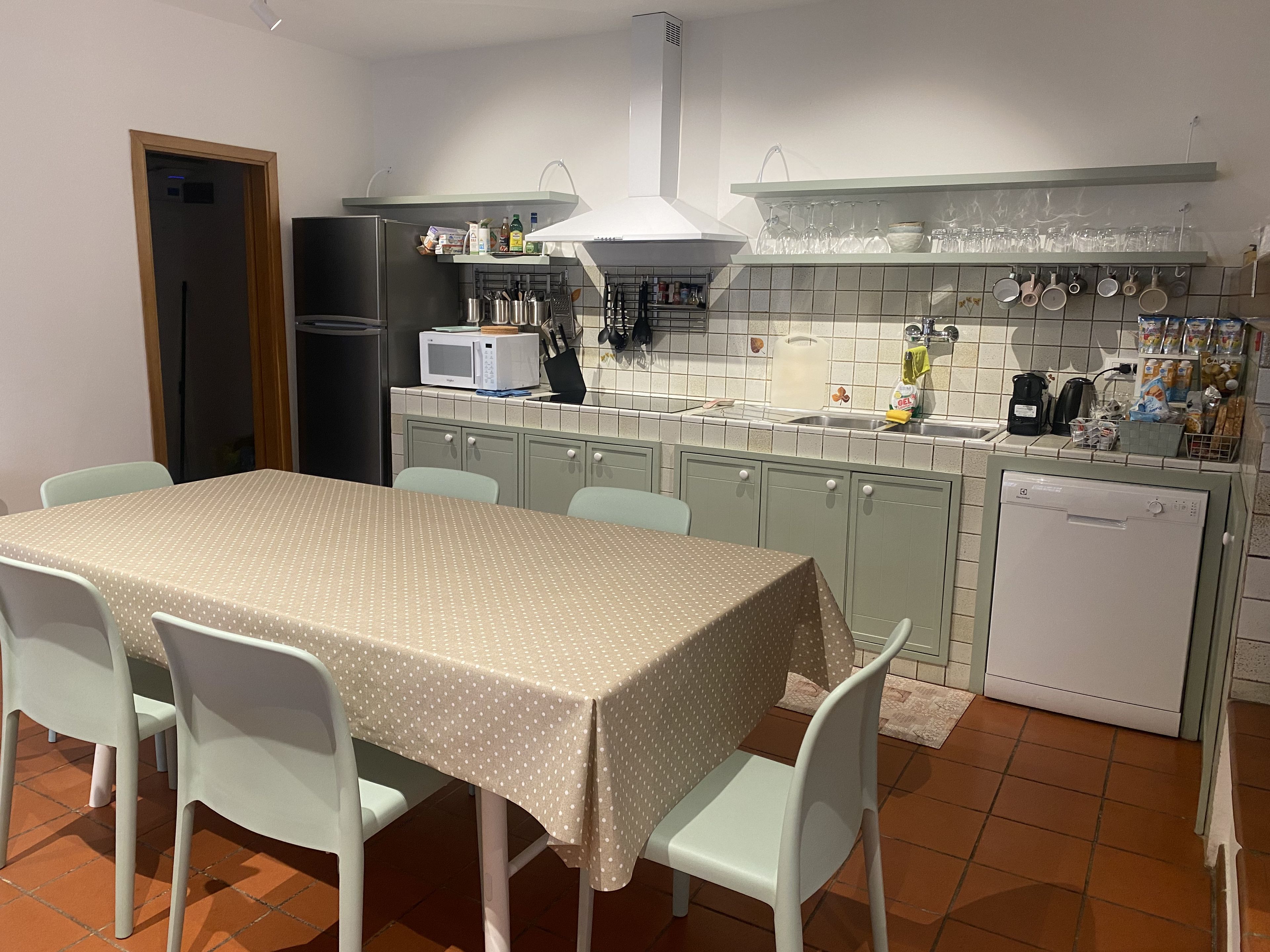 A kitchen with a dining table, chairs, a refrigerator, microwave, sink, and various kitchen utensils.