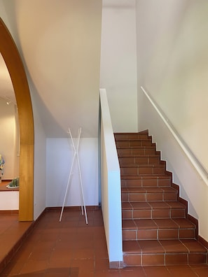 A staircase with brown tiles and a white handrail, leading to a landing with a white wall and a wooden archway. - Villanova 4 rooms  (Villanova)