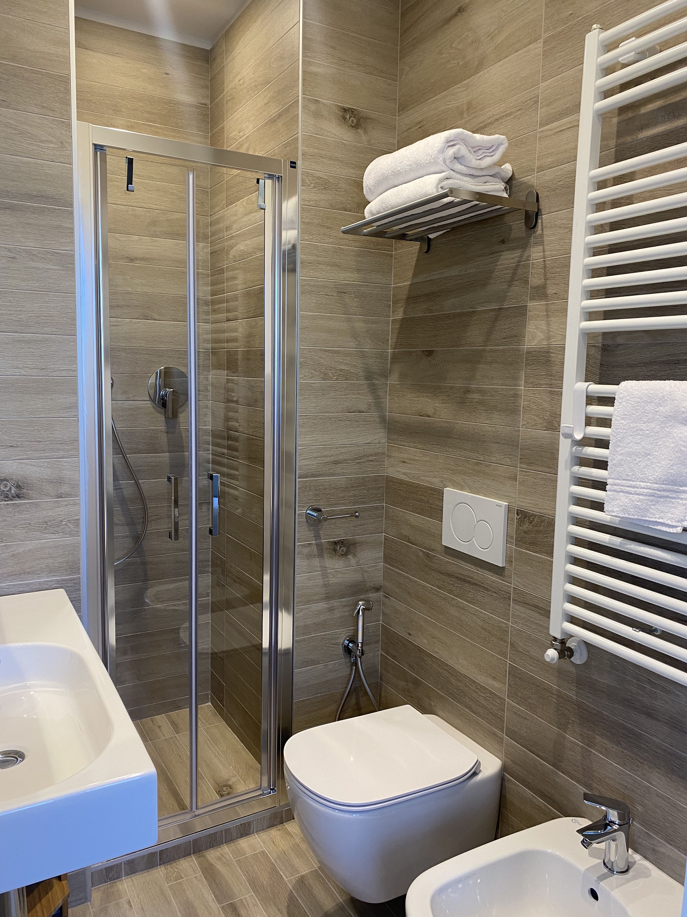 Ein modernes Badezimmer mit einer gläsernen Dusche, einer weißen Toilette, einem Bidet und einem Handtuchhalter.