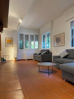 A spacious living room with two grey sofas, a round coffee table, and a large window with blinds. - Villanova 4 rooms  (Villanova)