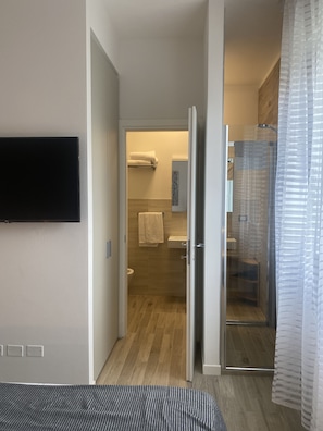 A hotel room with a bed, a TV mounted on the wall, a shower area with a glass door, and a toilet. - Villanova 4 rooms  (Castenaso)