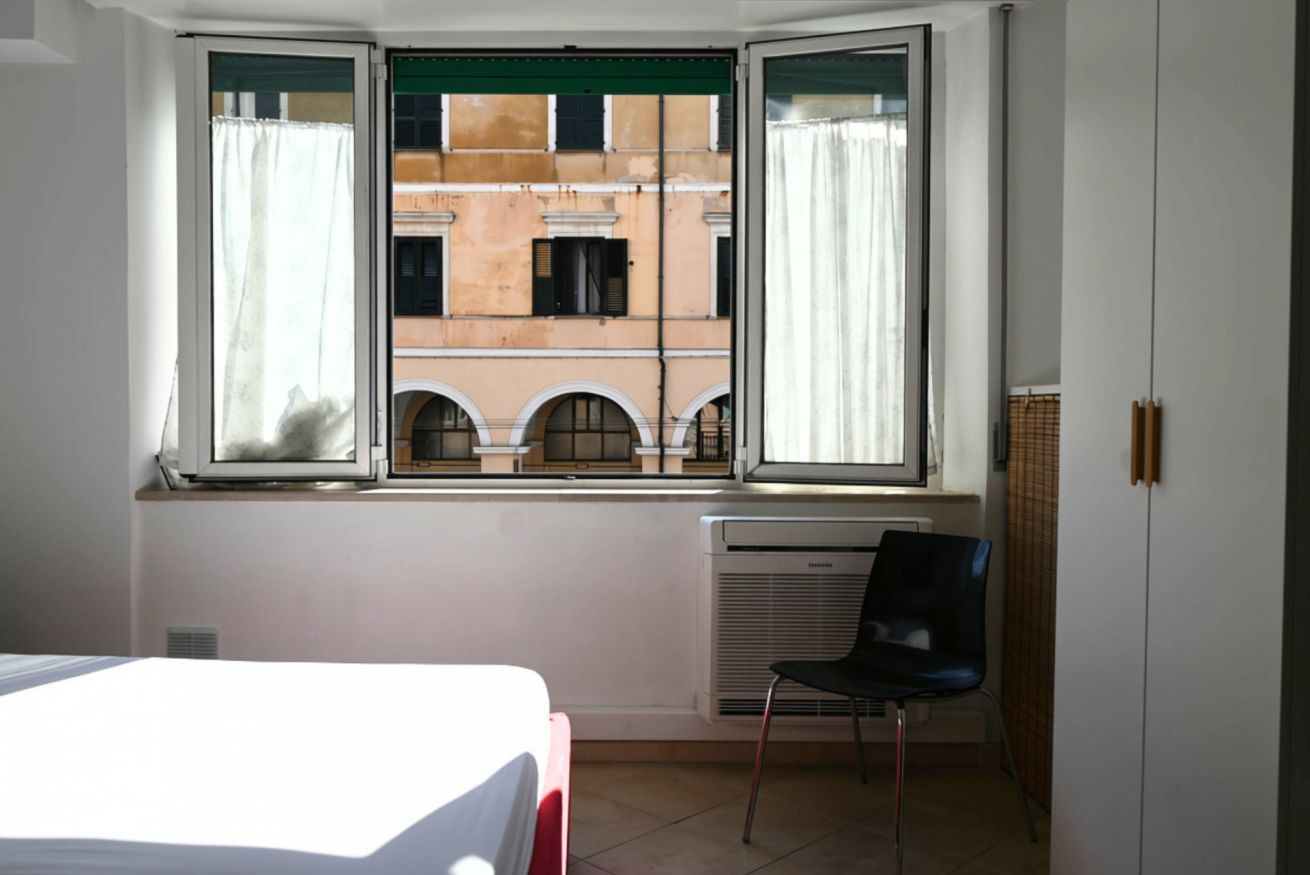 Una habitación con cama, una silla, un radiador y una ventana con cortinas.