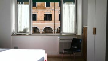 Una habitación con cama, una silla, un radiador y una ventana con cortinas.